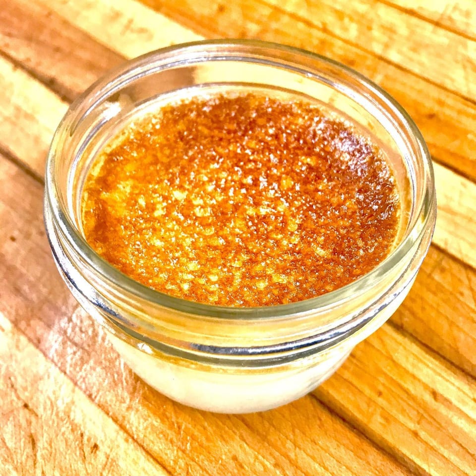 A glass ramekin of crème brûlée with a perfectly caramelized sugar topping on a wooden surface.