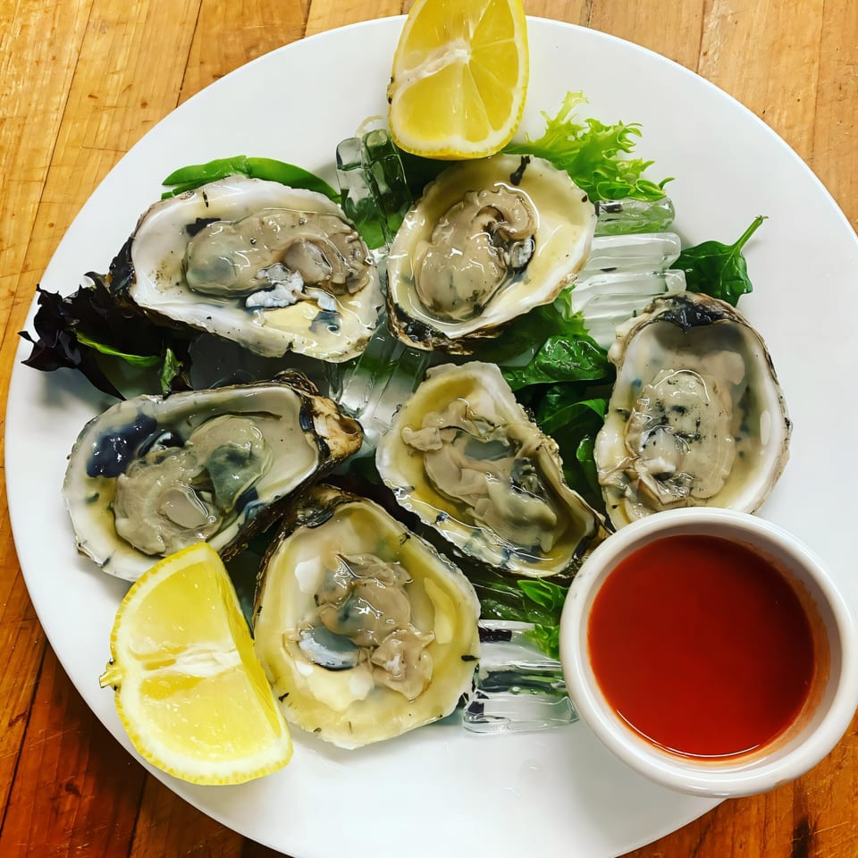Six fresh oysters on the half shell with ice, lemon wedges, and cocktail sauce.
