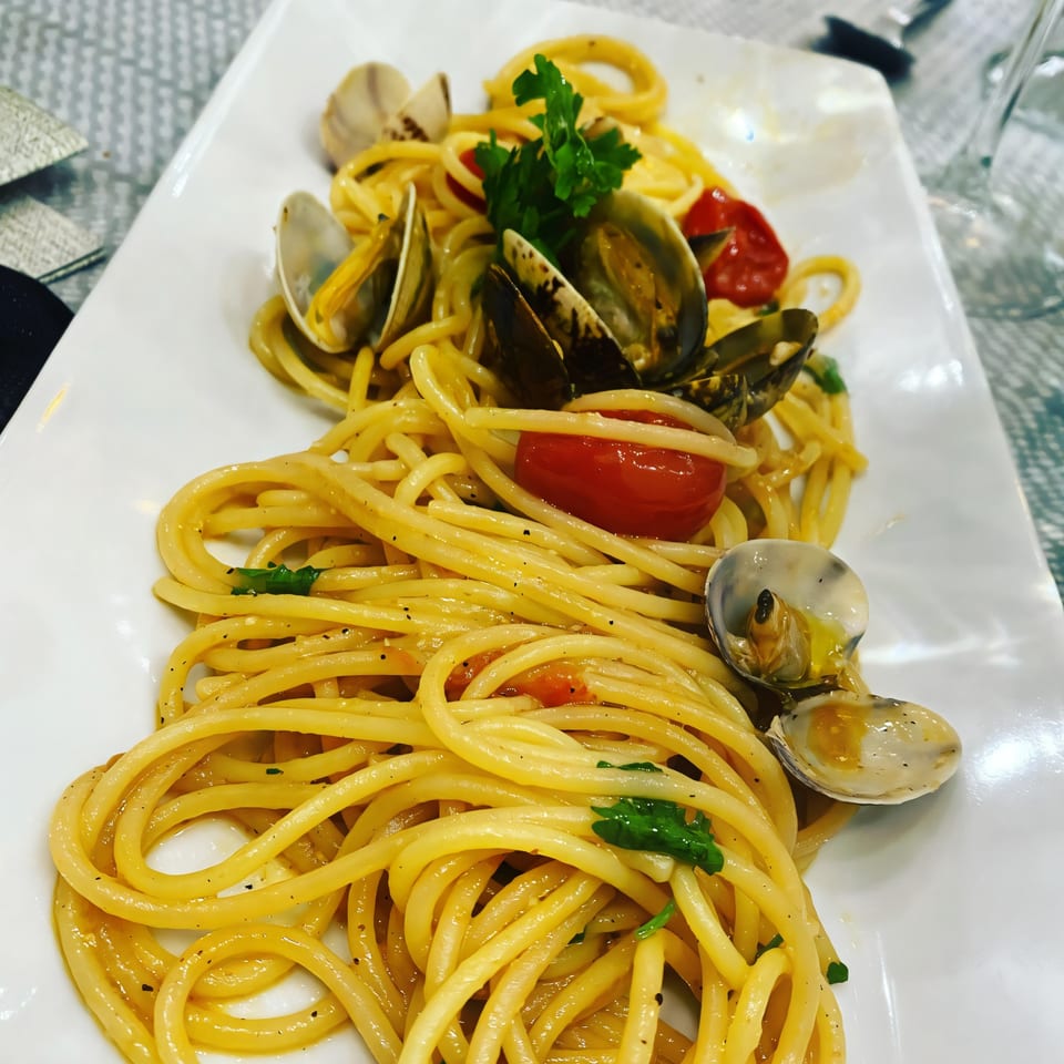 Spaghetti with clams, cherry tomatoes, and parsley on a white rectangular plate at Alfredo's Pizza.