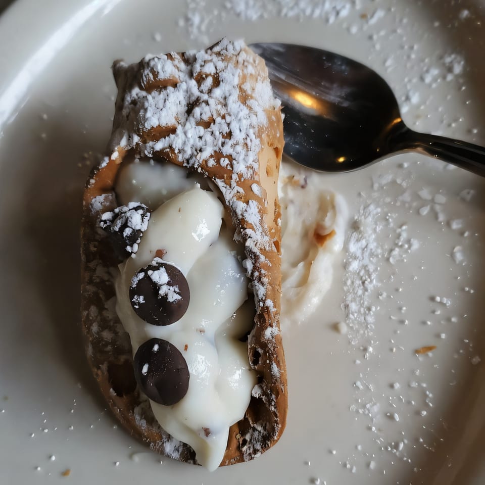 A cannoli from Alfredo's Pizza, filled with cream and chocolate chips, dusted with powdered sugar.