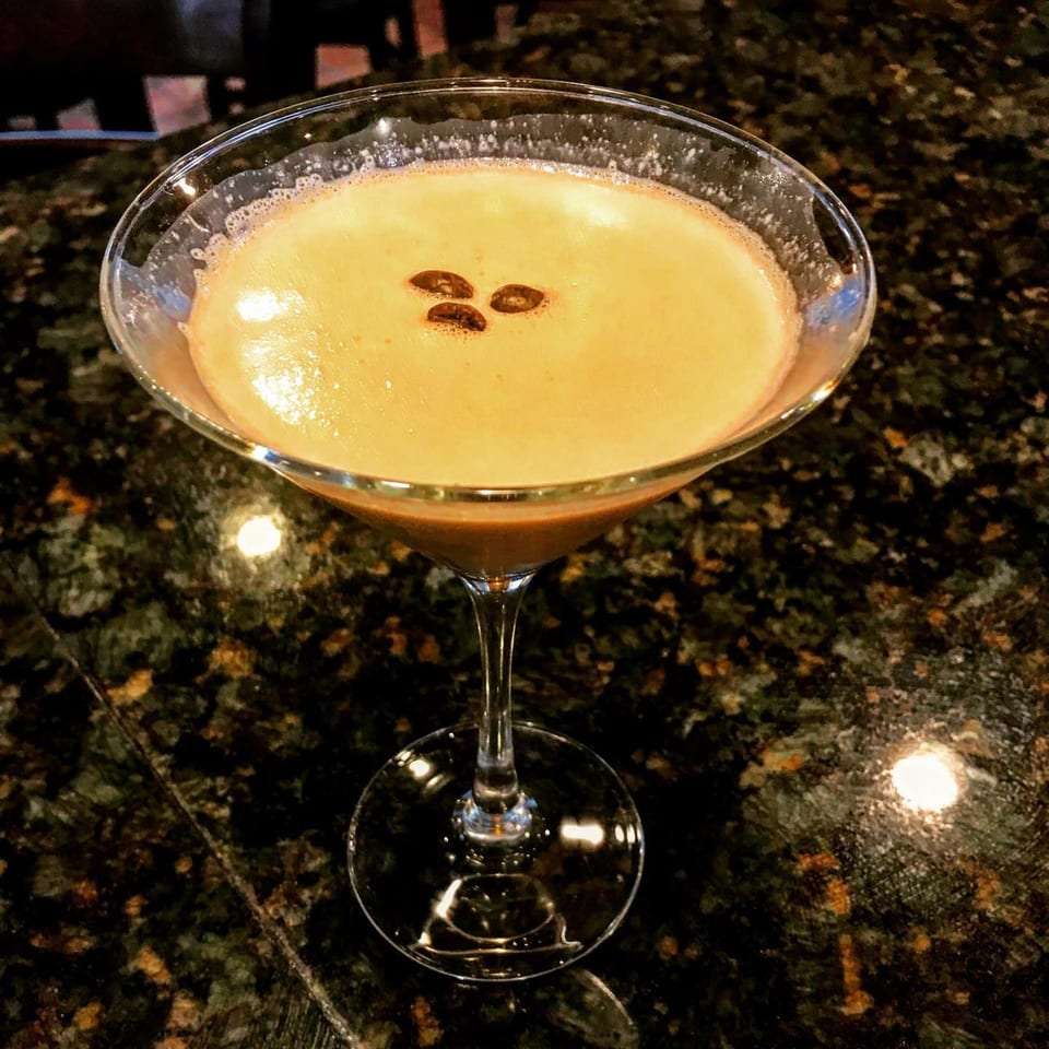 An espresso martini in a stemmed glass, garnished with three coffee beans on a dark granite surface.