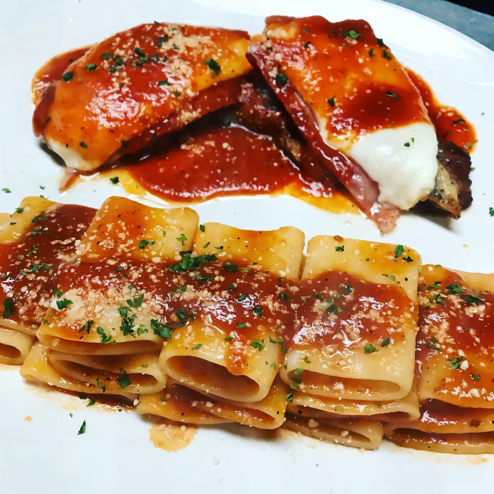 Two Italian dishes on a white plate: pasta with red sauce and two stuffed rolls with red sauce.